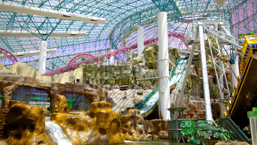 Área interna de parque de diversos com montanha russa e teto com estruturas coloridas e entrada com luz natural