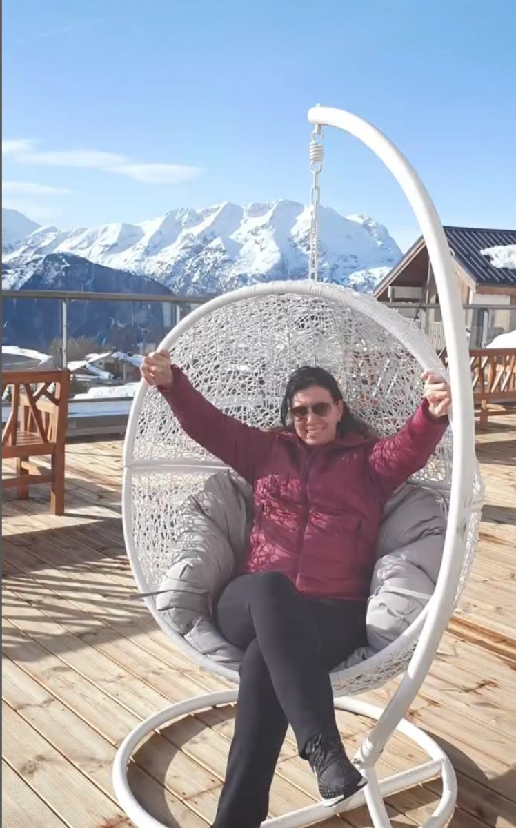 mulher sentada em cadeira de balanço em deck com montanhas de neve ao fundo